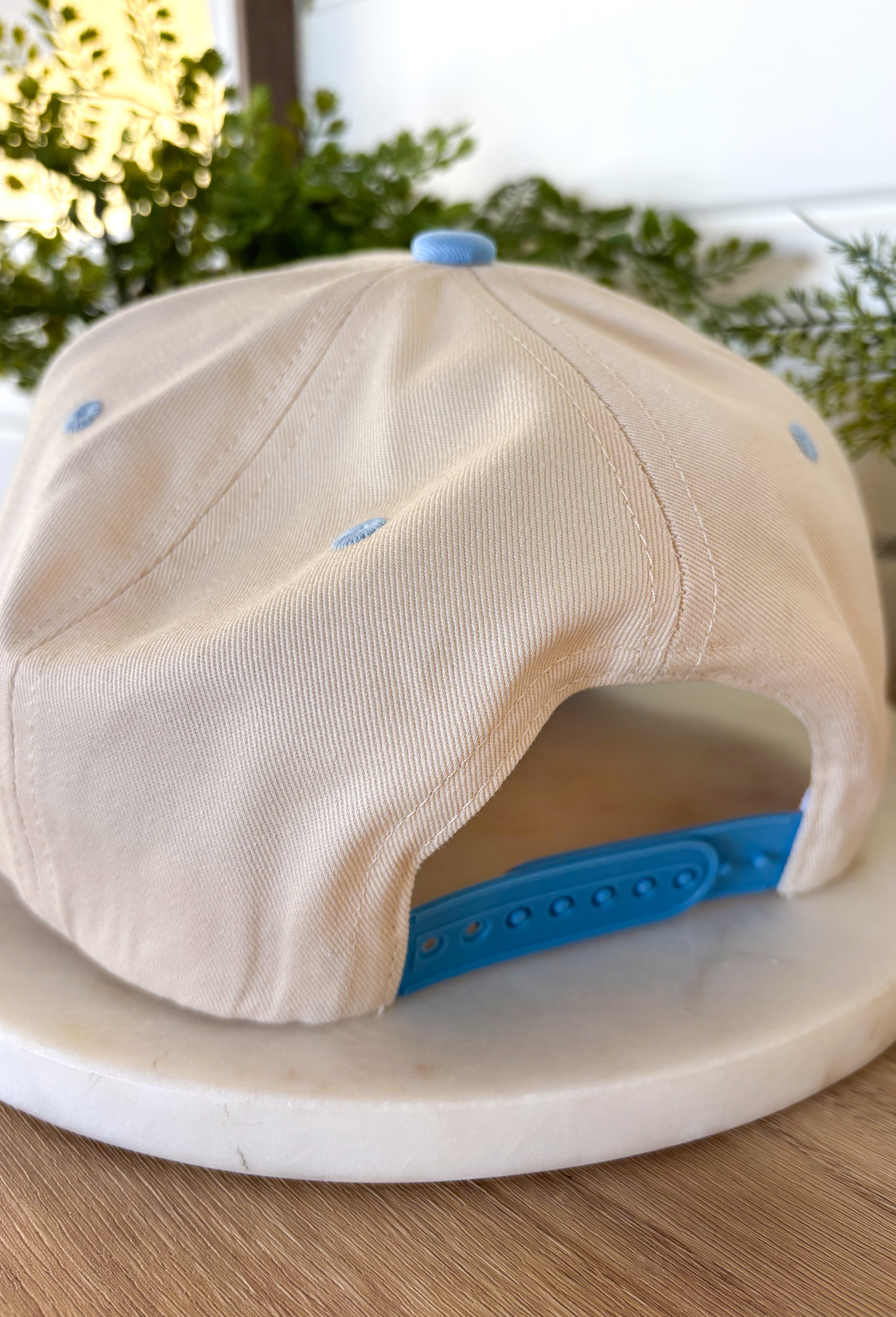 This neutral trucker hat is finished with a soft light blue bill for a fresh, easygoing look. Featuring an embroidered western-inspired design on the front, it adds just the right amount of character while staying effortlessly wearable. The adjustable back ensures a comfortable fit, making it perfect for everyday errands, outdoor plans, or topping off a casual outfit.