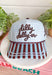 Bring a little fun to your everyday look with this charming trucker hat that's full of playful personality. Featuring a light blue and white gingham front paired with a light blue and brown striped bill, this unique hat is finished with white embroidered detailing along the bill for an extra touch of texture. The front is embroidered in chocolate brown with "Dilly Dally-er," while the side proudly reads "World's Best" with a ribbon. 
