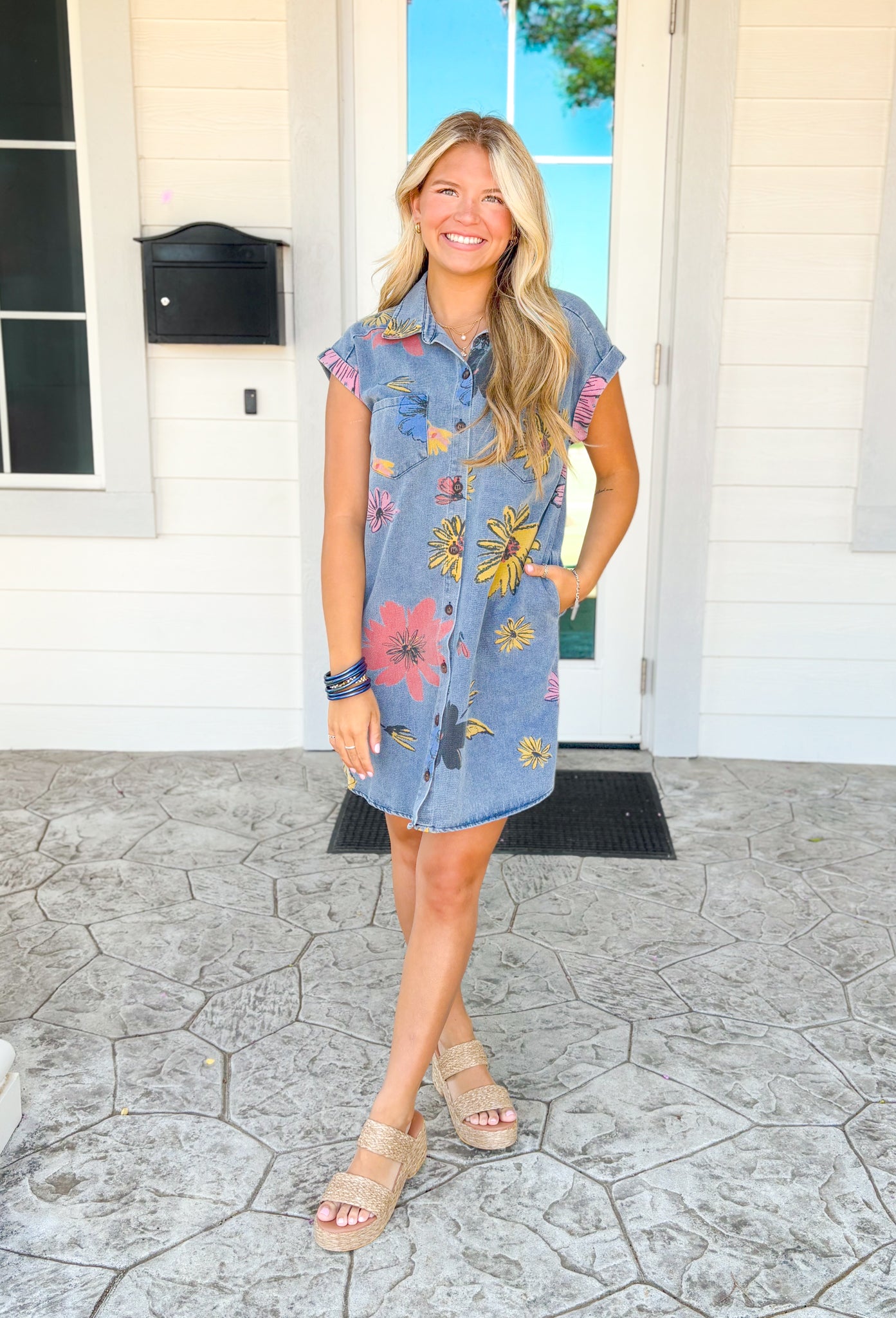 Feels Like Summer Dress, medium wash short sleeve button down denim dress with two pockets on the chest and pockets, pinkish red, yellow, and blue enlarged floral design covering the dress with charcoal outlines 