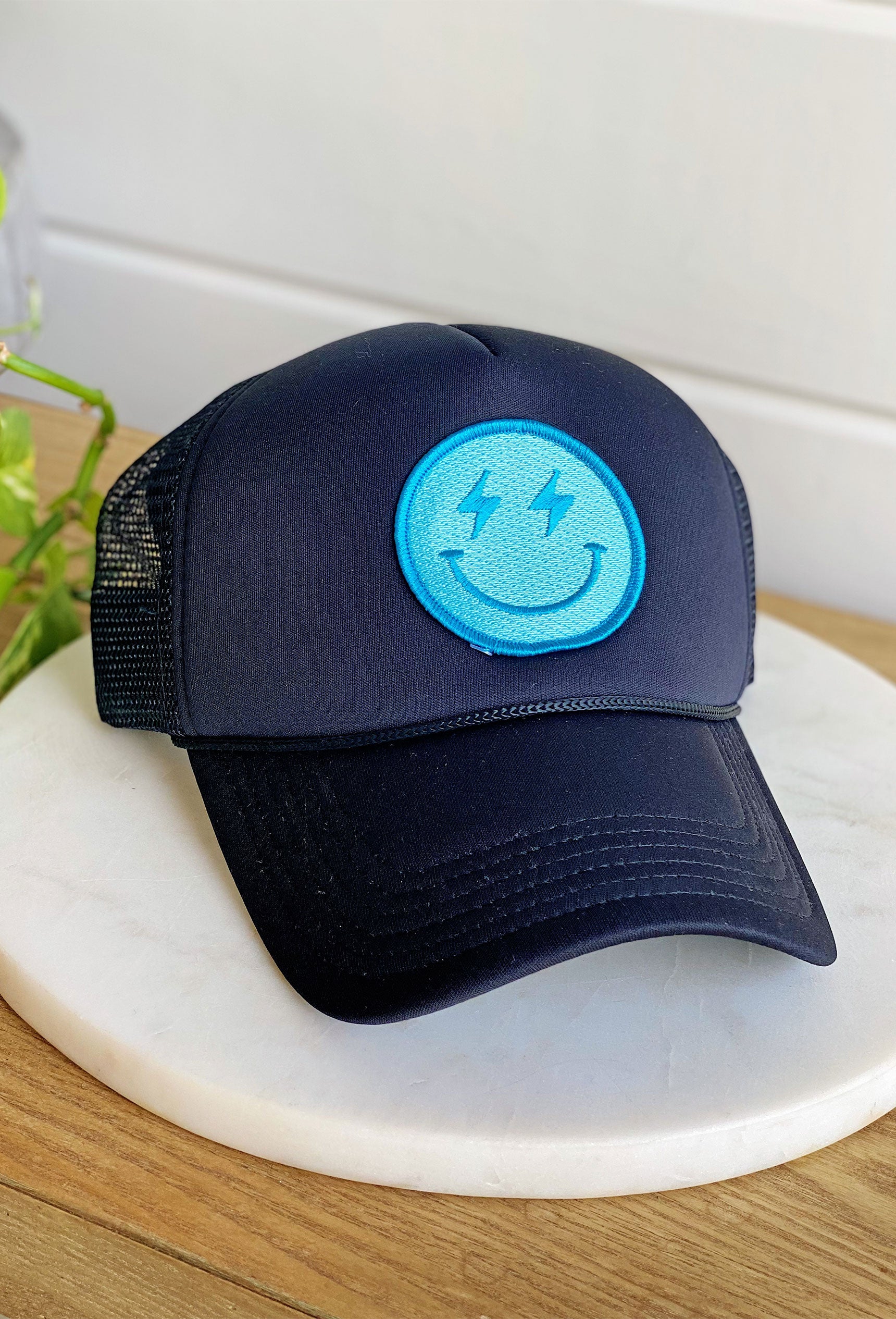 Happy Vibes Trucker Hat in Black, black hat with turquoise patch on front, smiley face with lightening bolt eyes, adjustable